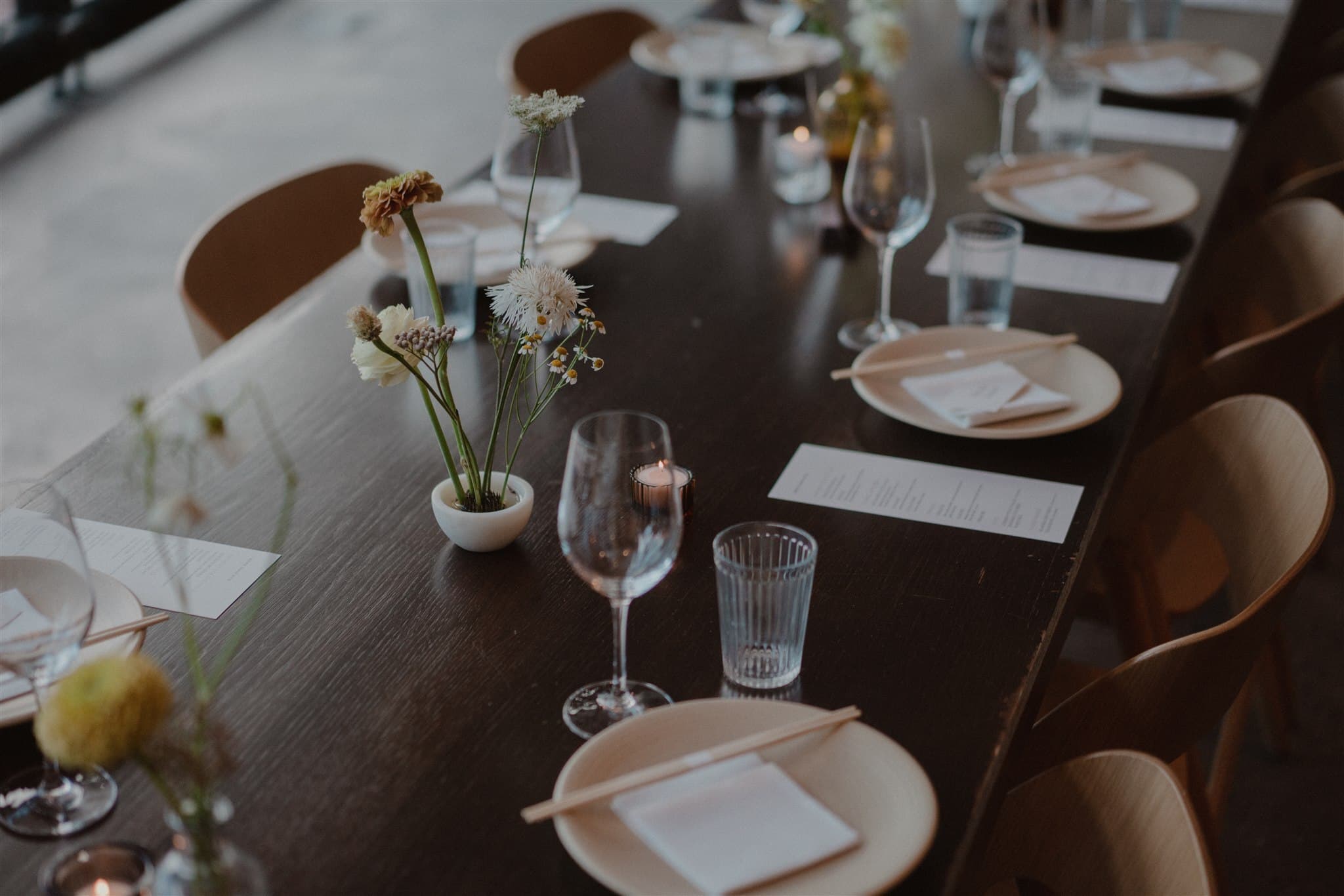 Intimate wedding dinner table set with wildflower arrangements, tapered candles, and wine glasses on a dark wood table, photo by Chellise Michael Photography