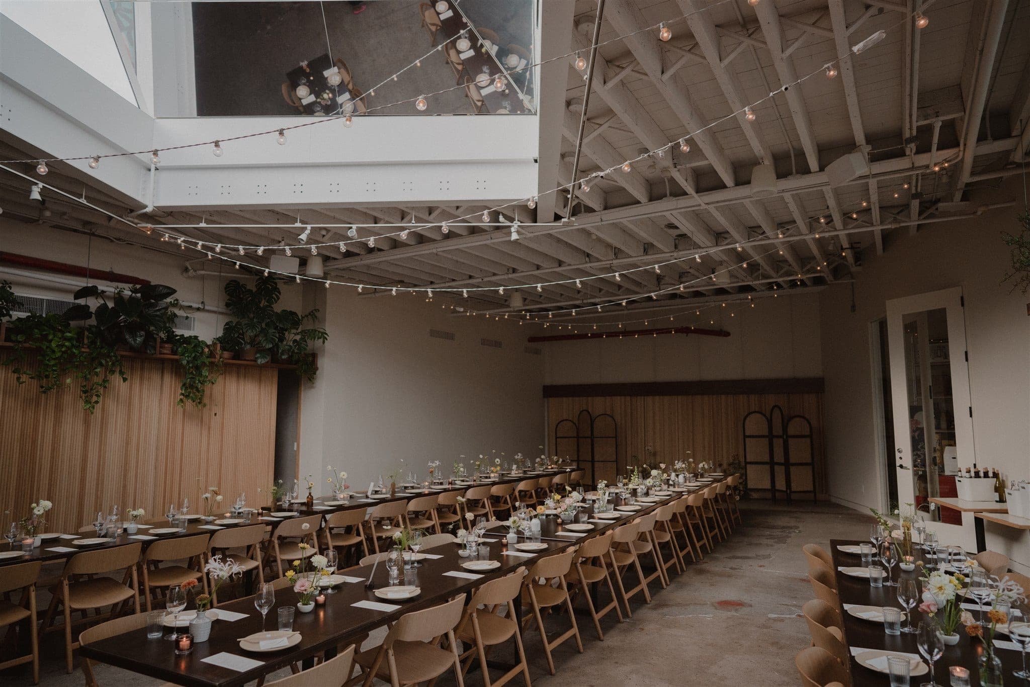 Spacious wedding reception venue with bistro string lights overhead and long family-style tables set for a seated dinner celebration, photo by Chellise Michael Photography